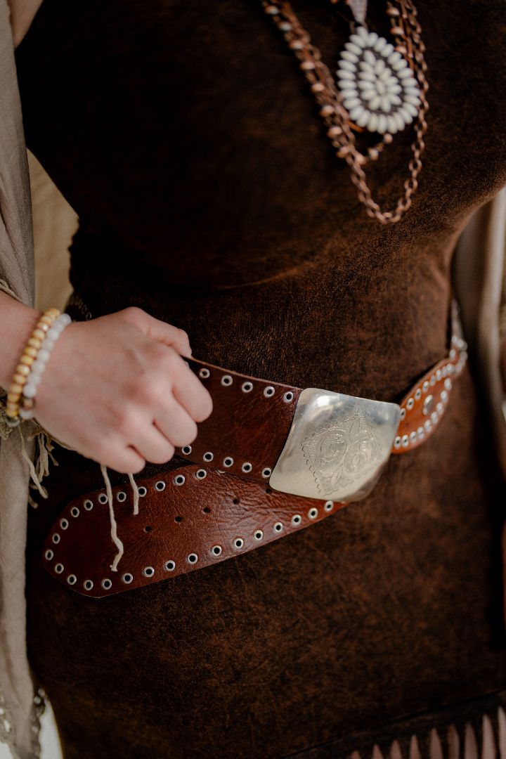 Person wearing a brown leather belt with a silver buckle, holding a beige bag.