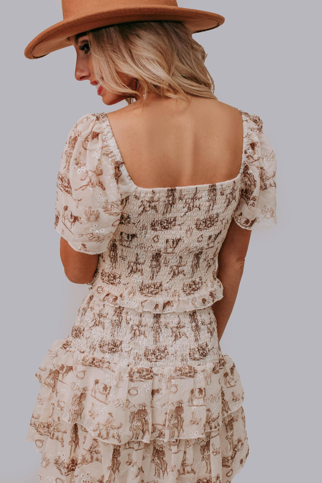 Woman wearing a floral dress and brown hat against a gray background